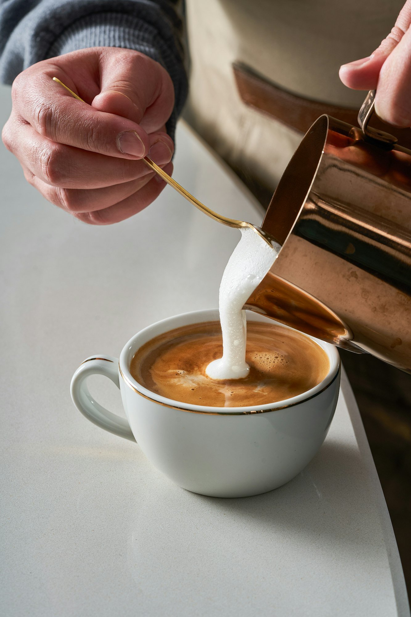 Close-up photo of a person preparing a cup of latte and coffee